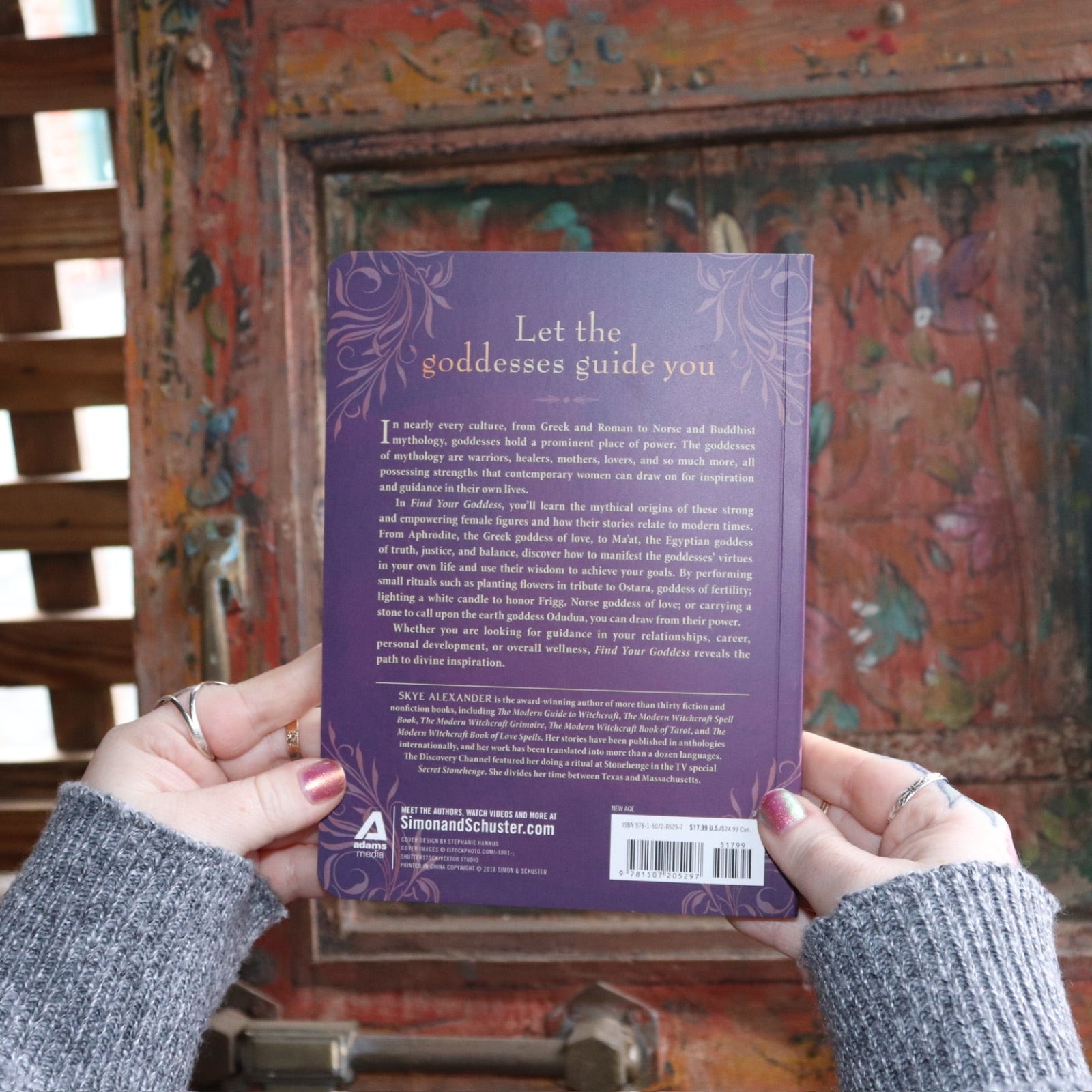 Someone holding the Find Your Goddess Paperback Book in front of a wood background, showing off the back.