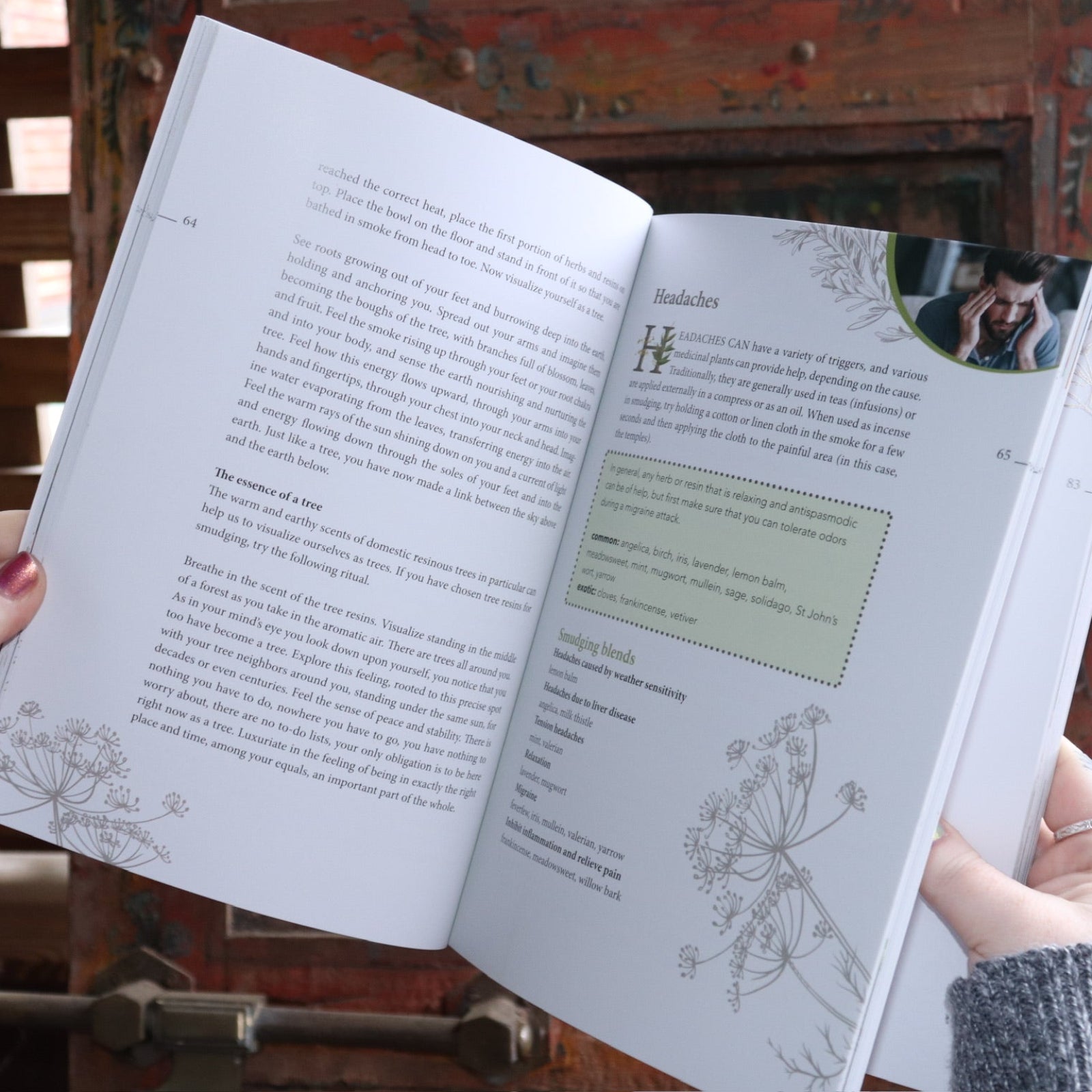 Someone holding the Complete Smudging Handbook Paperback Book open in front of a wooden background, showing off the pages.