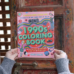 Someone holding the 1990s Coloring Book in front of a wooden background. 