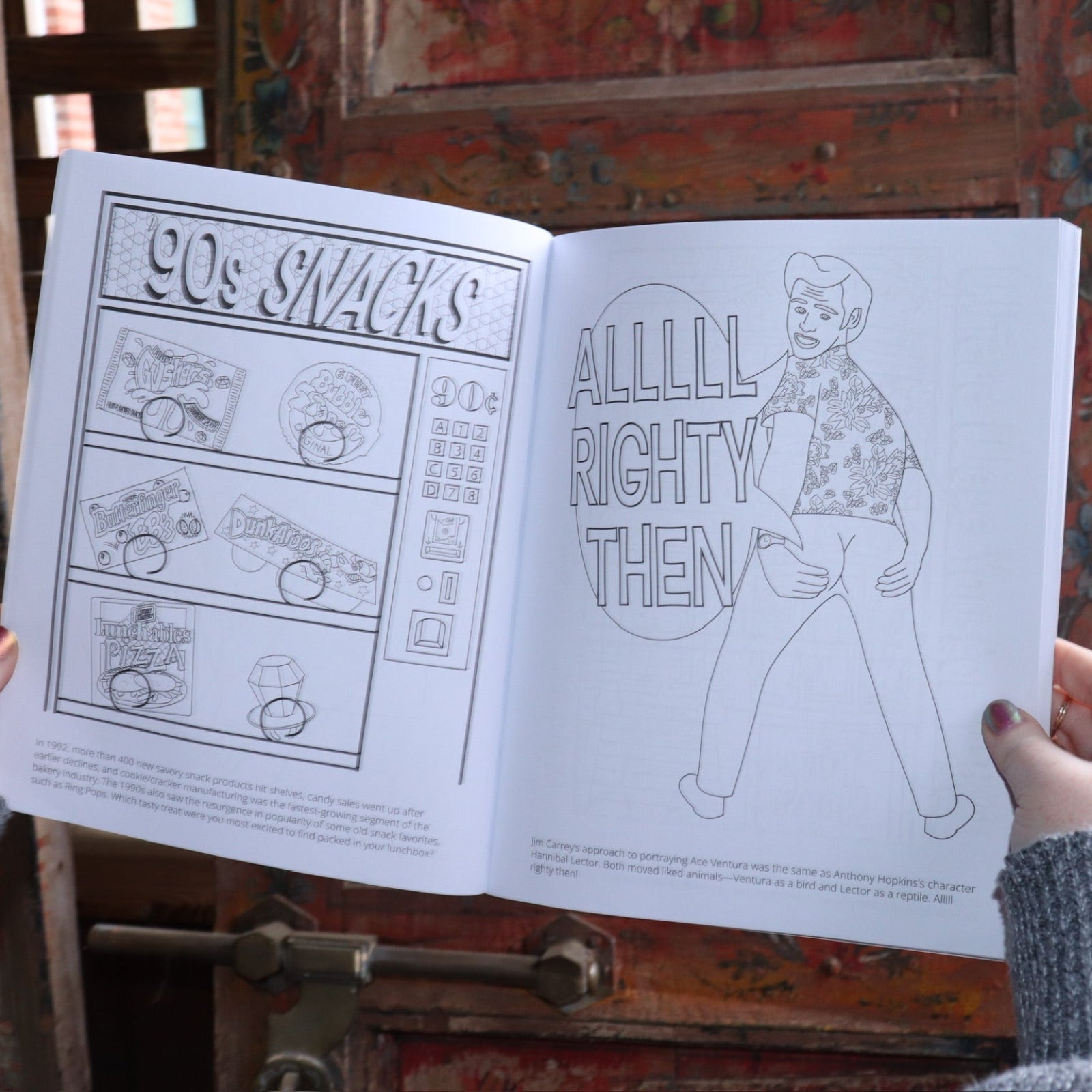 Someone holding the 1990s Coloring Book open in front of a wooden background, showing off the pages.