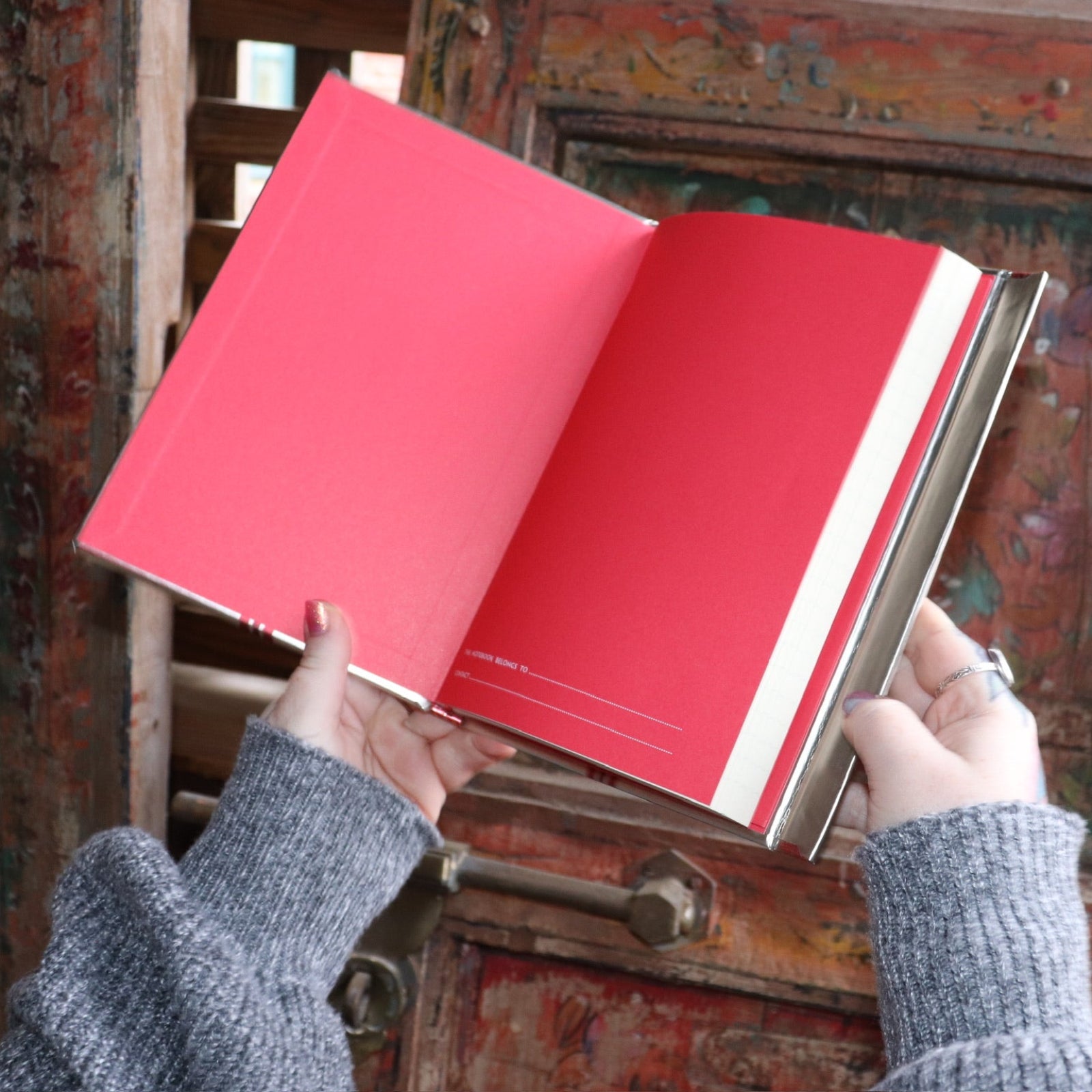 Someone holding the Love Oracle Foiled Hardcover Journal open in front of a wooden background.