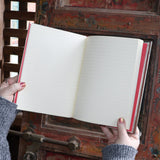 Someone holding the Love Oracle Foiled Hardcover Journal open in front of a wooden background, showing off the pages.
