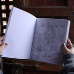 Someone holding the Golden Girls Color-by-Number Coloring Book open in front of a wooden background, showing off the pages.