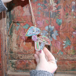 Someone holding the Recycled Magazine Mushroom Ornament in front of a colorful wooden background.