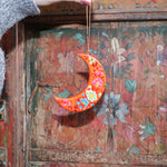 Someone holding a Papier-mâché Hand-Painted Moon Ornament in front of a colorful wooden background.