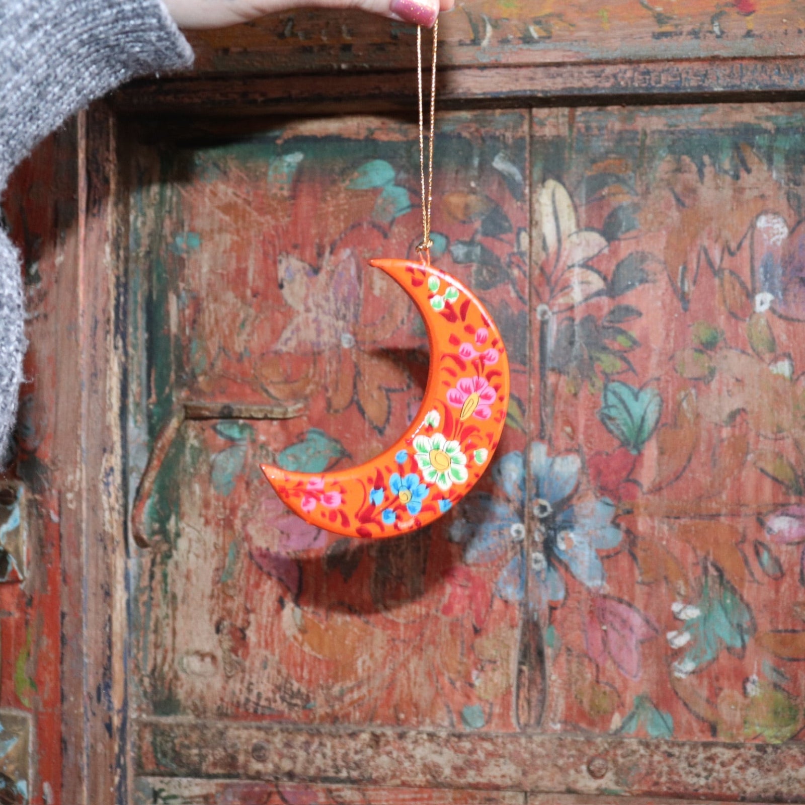 Someone holding a Papier-mâché Hand-Painted Moon Ornament in front of a colorful wooden background.