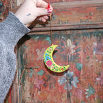 Someone holding a Papier-mâché Hand-Painted Moon Ornament in front of a colorful wooden background.
