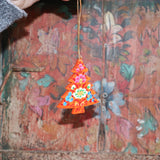 The Papier-mâché Hand-Painted Tree Ornament being held in front of a colorful wooden background.