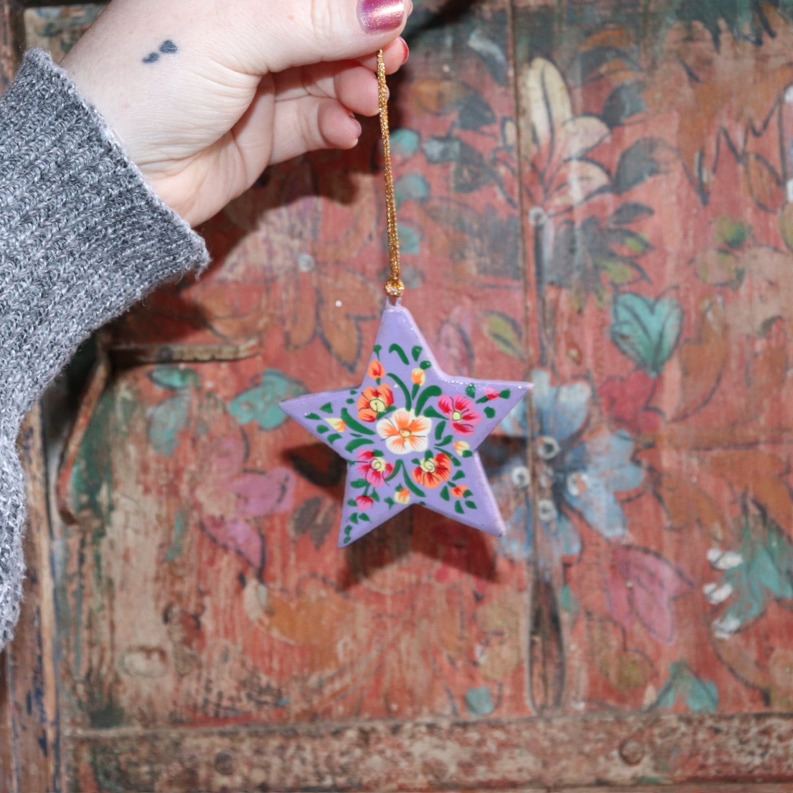 Someone holding a Papier-mâché Hand-Painted Star Ornament in front of a colorful wooden background.