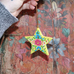 Someone holding a Papier-mâché Hand-Painted Star Ornament in front of a colorful wooden background.