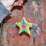 Someone holding a Papier-mâché Hand-Painted Star Ornament in front of a colorful wooden background.