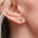 Someone wearing the gold Memento Mori Mini Skull Stud Earrings.