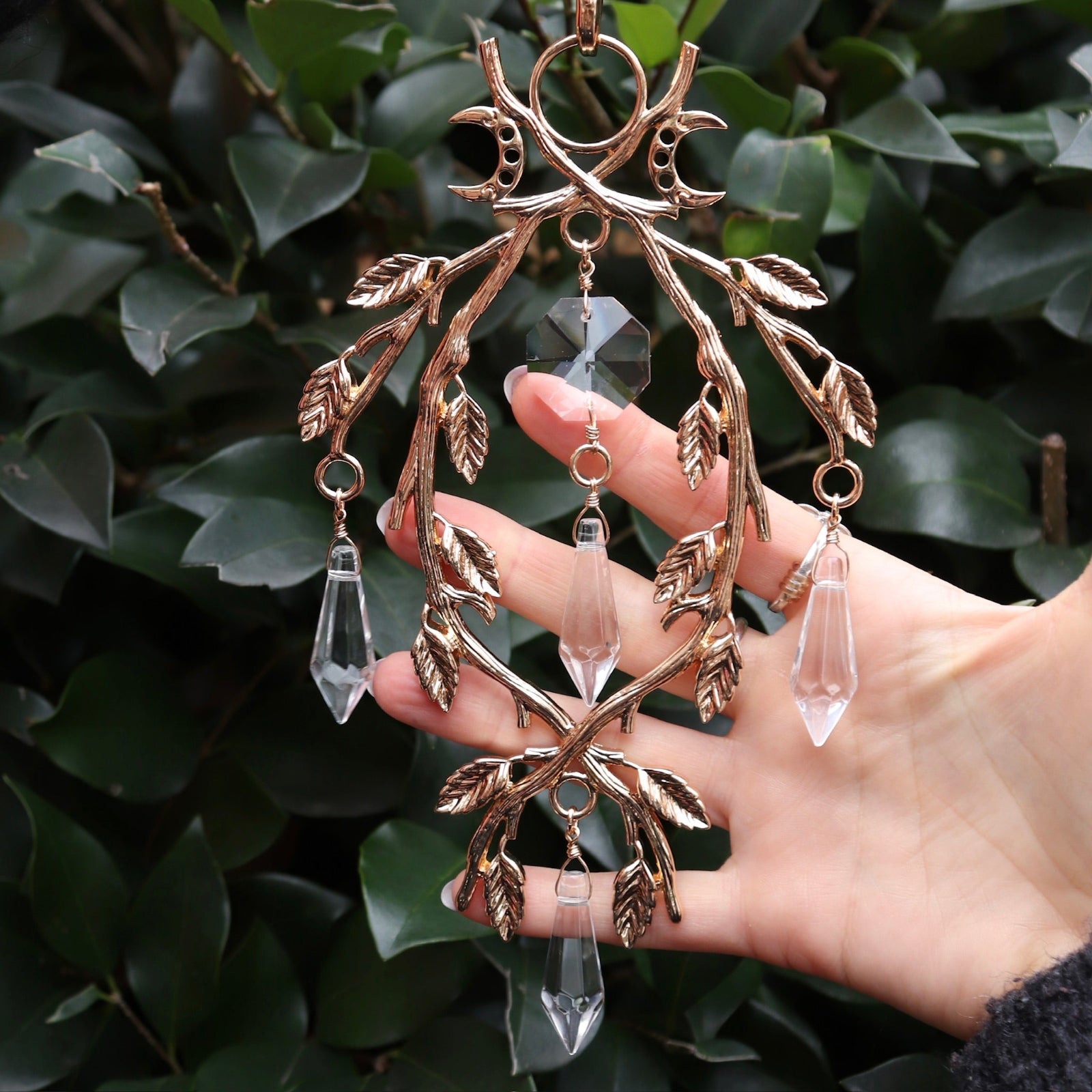 Someone holding the Faerie Gold Suncatcher in front of a green bush.