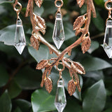 An up-close image of someone holding the Faerie Gold Suncatcher in front of a green bush.