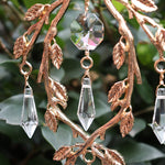 An up-close image of someone holding the Faerie Gold Suncatcher in front of a green bush.