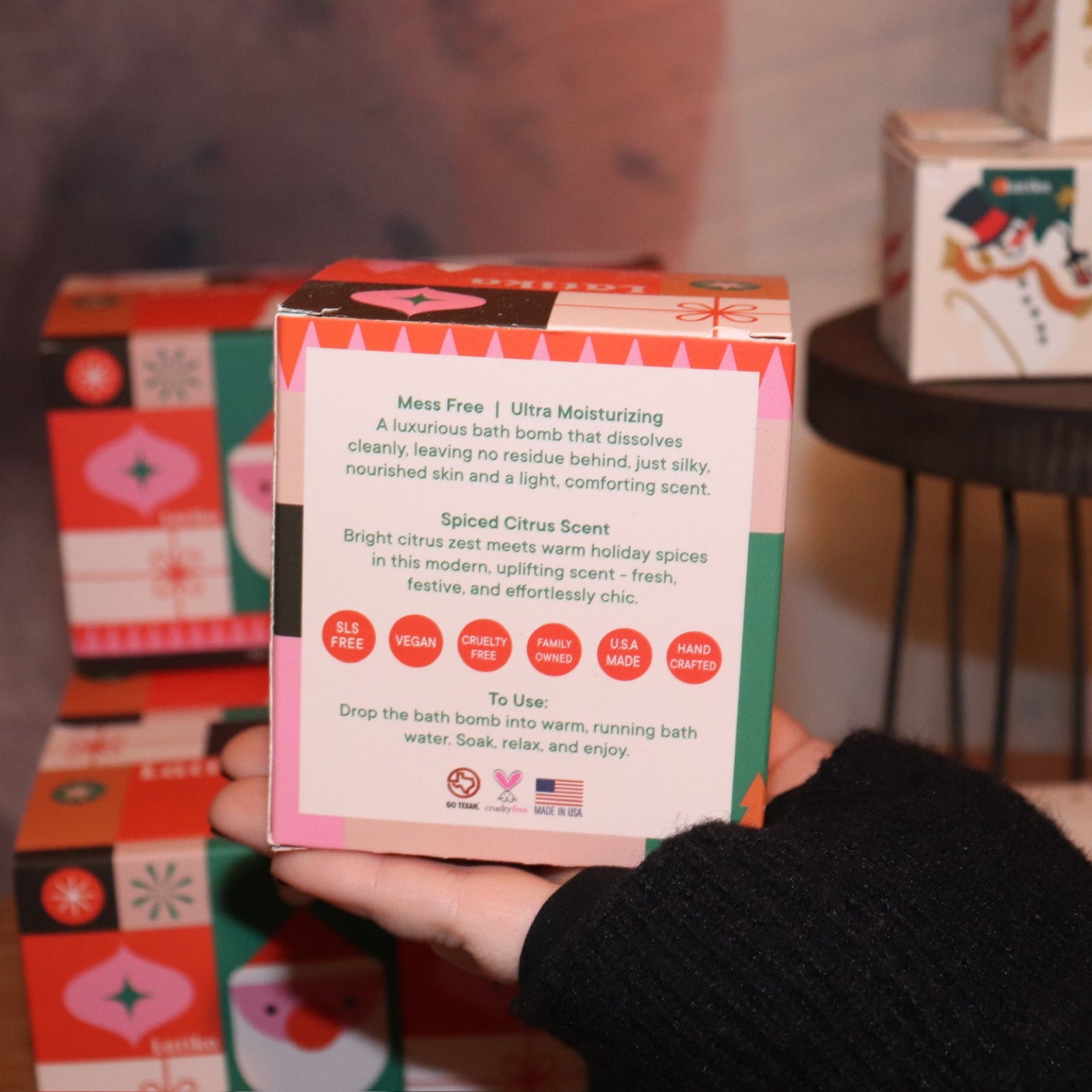 Someone holding the Geometric Santa Bath Bomb in front of other bath bombs, showing off the back.