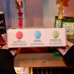 Someone holding the Holiday Christmas Bath Bomb Set in front of a colorful background, showing off the back.