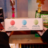 Someone holding the Holiday Christmas Bath Bomb Set in front of a colorful background, showing off the back.