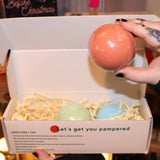 Someone holding the Holiday Christmas Bath Bomb Set in front of a colorful background, showing the inside with someone holding one of the bath bombs.