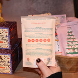 Someone holding the Snow Bath Soak in front of other bath products, showing off the back.