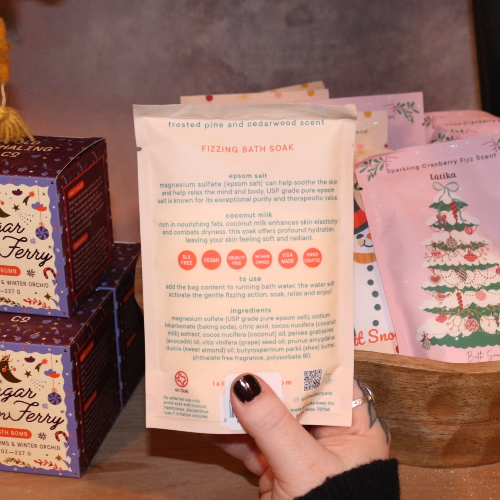 Someone holding the Snow Bath Soak in front of other bath products, showing off the back.