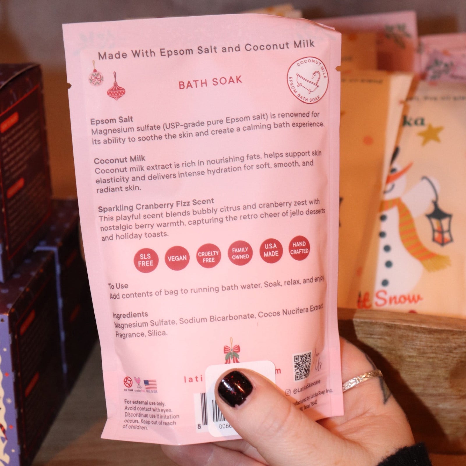 Someone holding a Pink Christmas Tree Bath Soak in front of other bath holiday products, showing off the back.