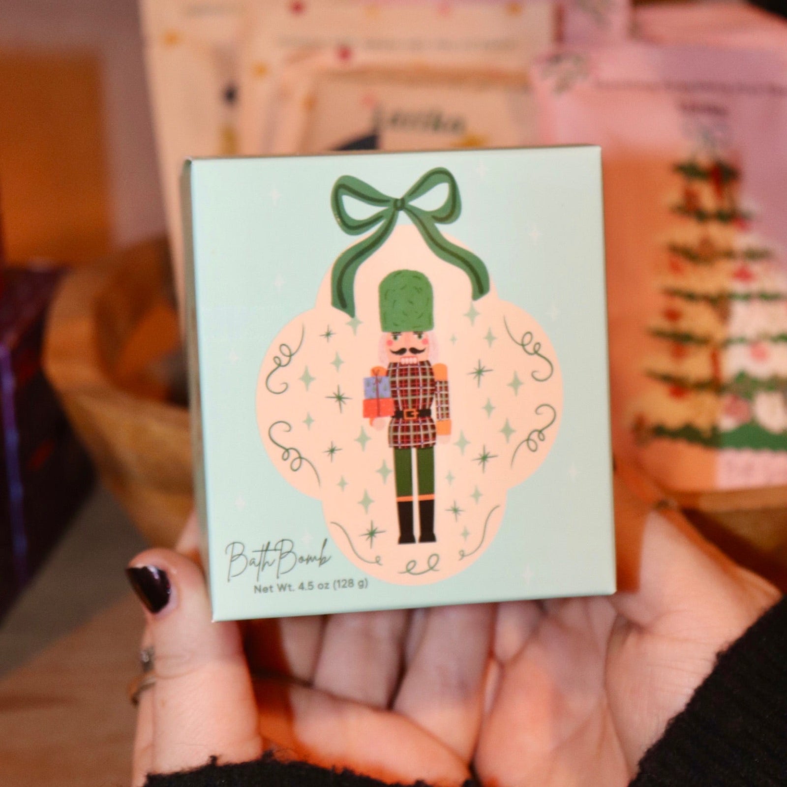 Someone holding the Nutcracker Bath Bomb in front of other holiday bath products.