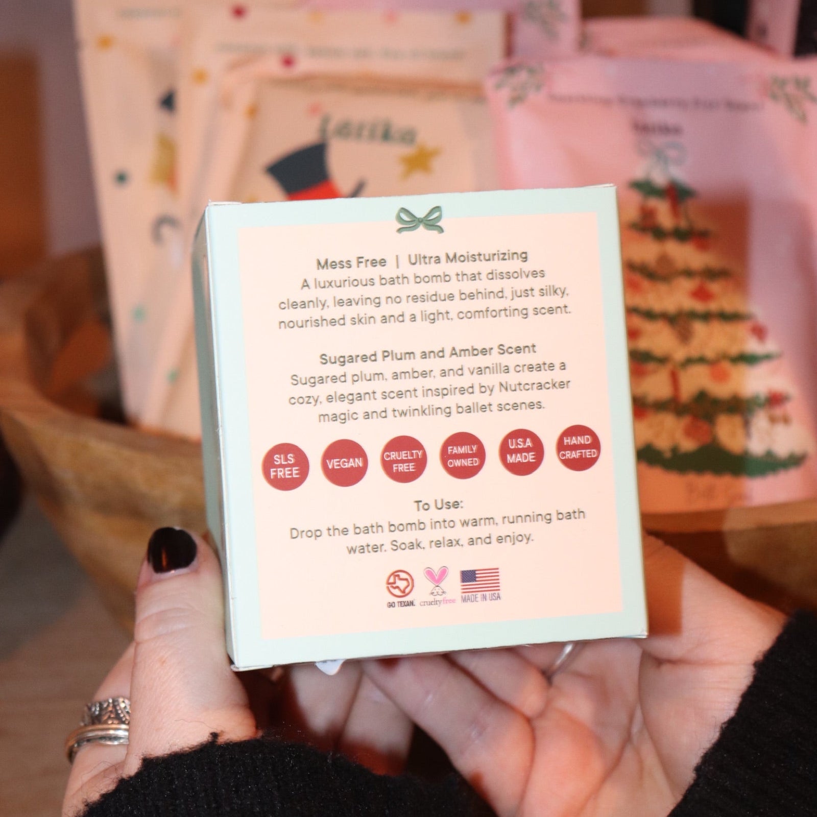 Someone holding the Nutcracker Bath Bomb in front of other holiday bath products, showing off the back.