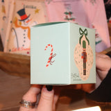 Someone holding the Nutcracker Bath Bomb in front of other holiday bath products, showing off the side.