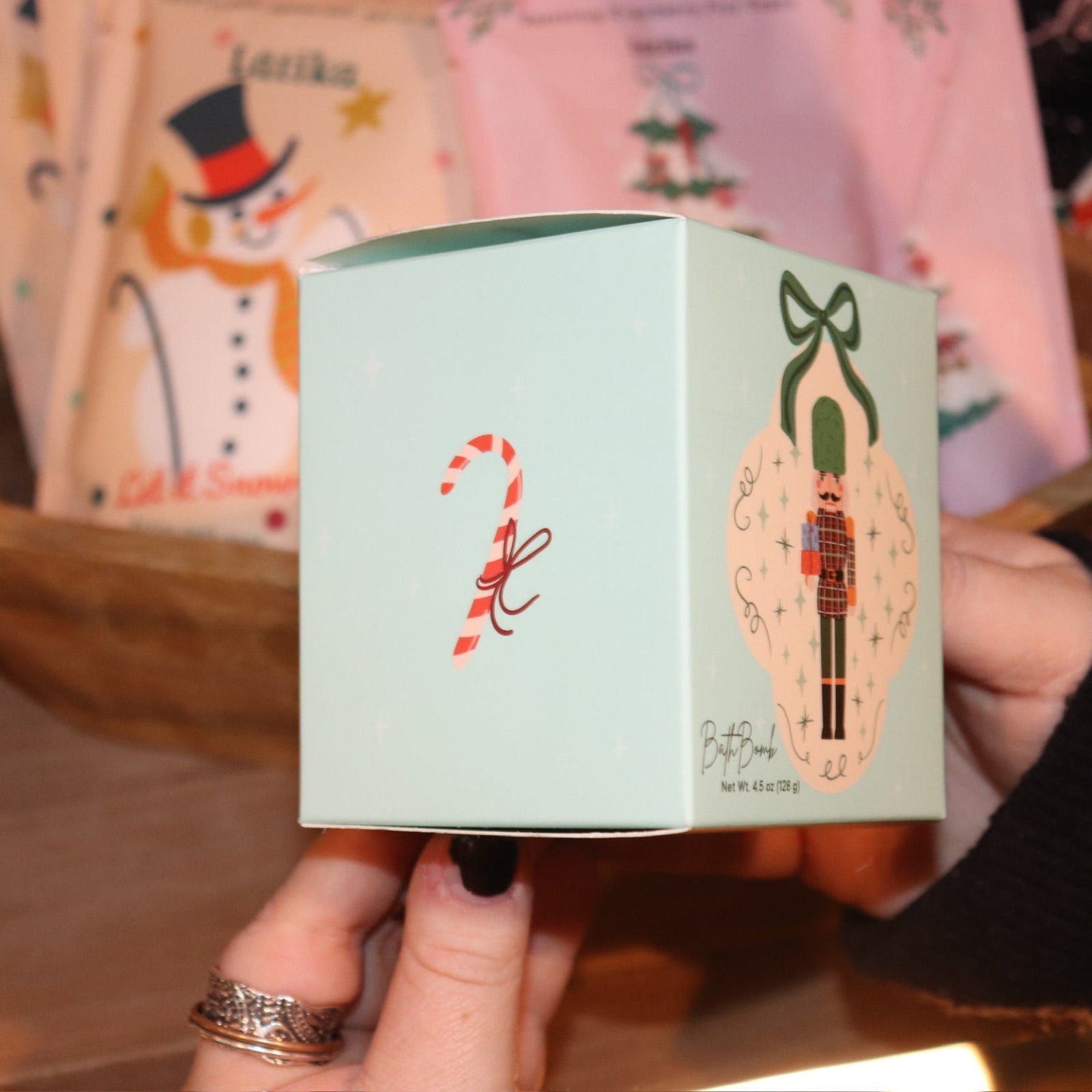 Someone holding the Nutcracker Bath Bomb in front of other holiday bath products, showing off the side.