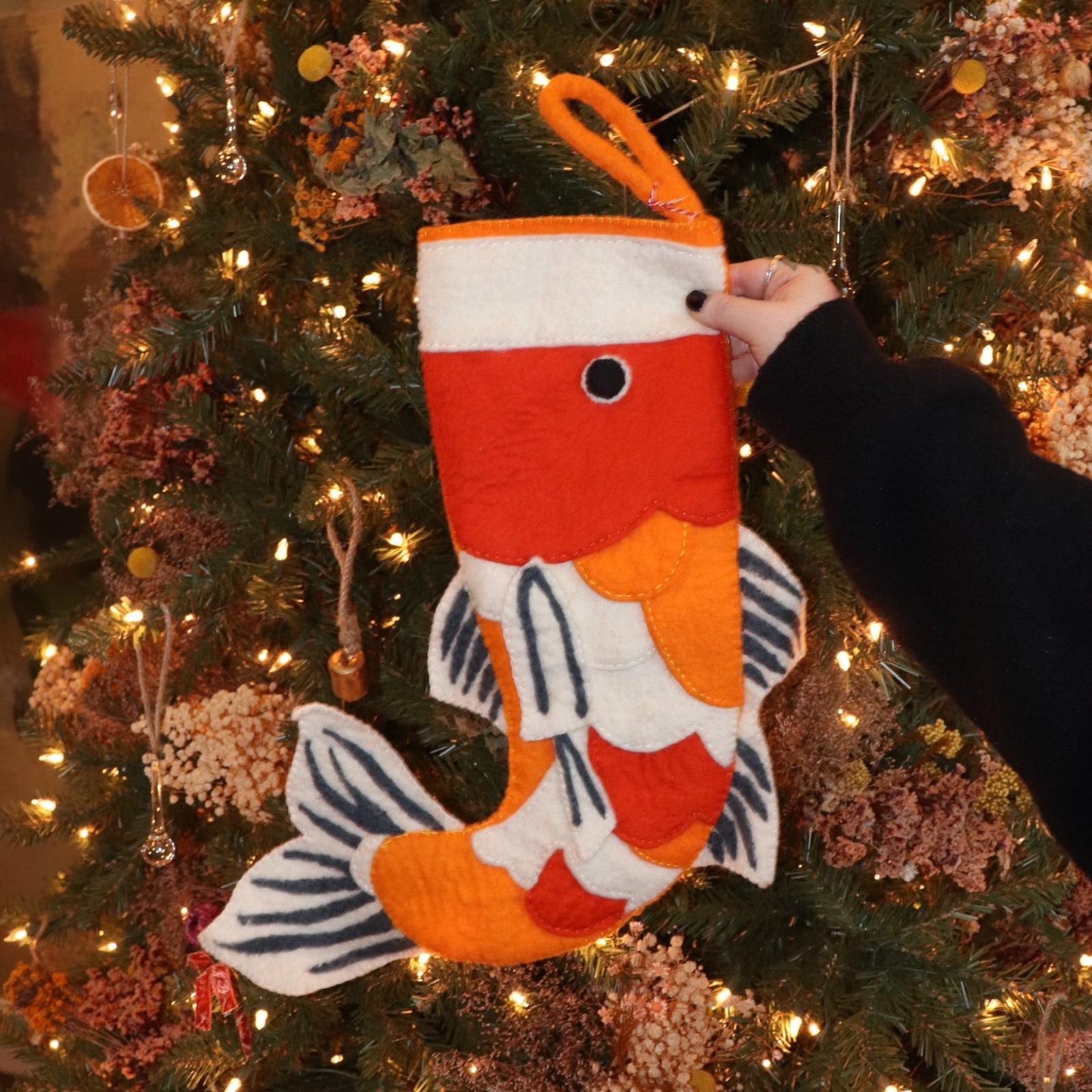 Someone holding the Felt Japanese Koi Fish Christmas Stocking in front of a Christmas tree.