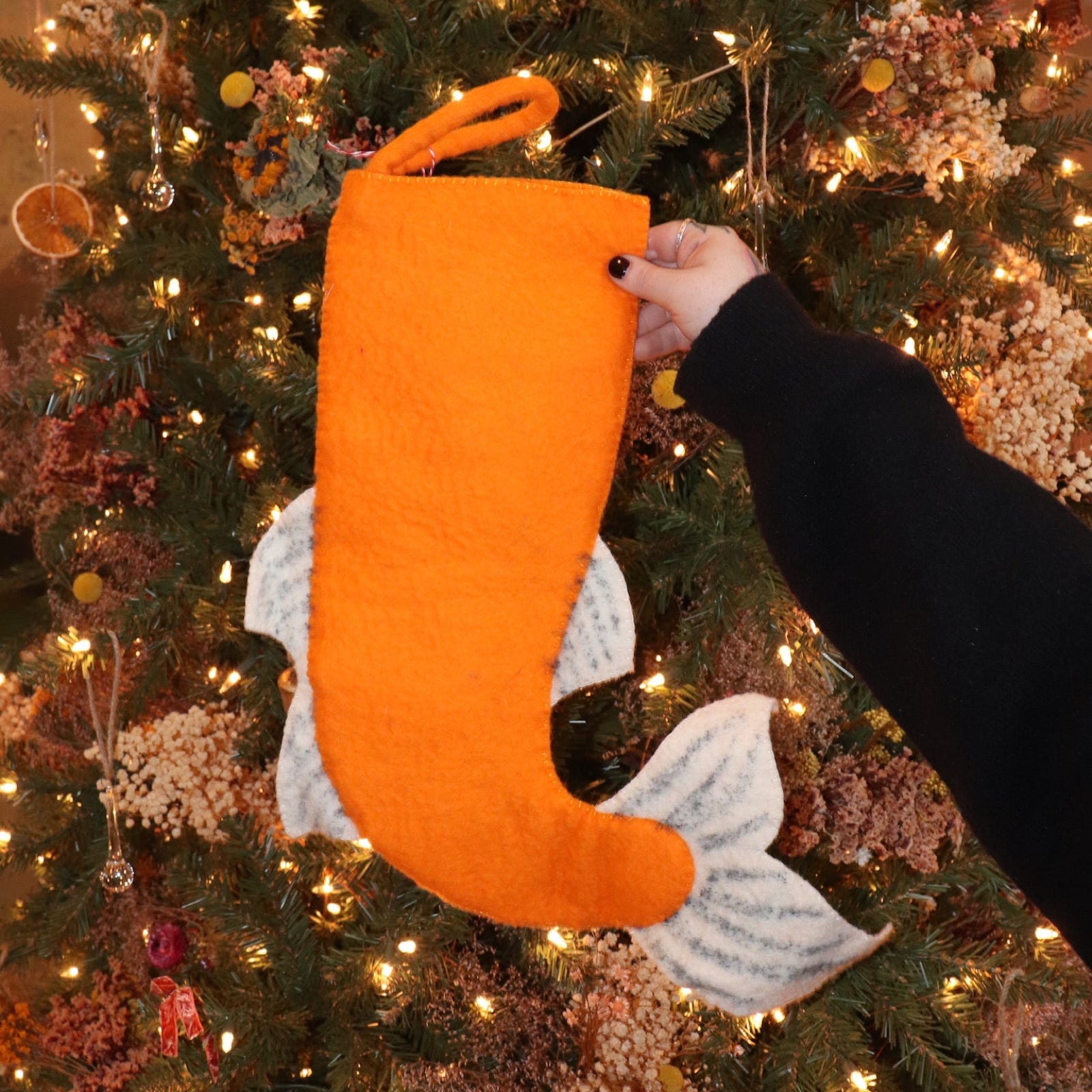Someone holding the Felt Japanese Koi Fish Christmas Stocking in front of a Christmas tree, showing off the back.
