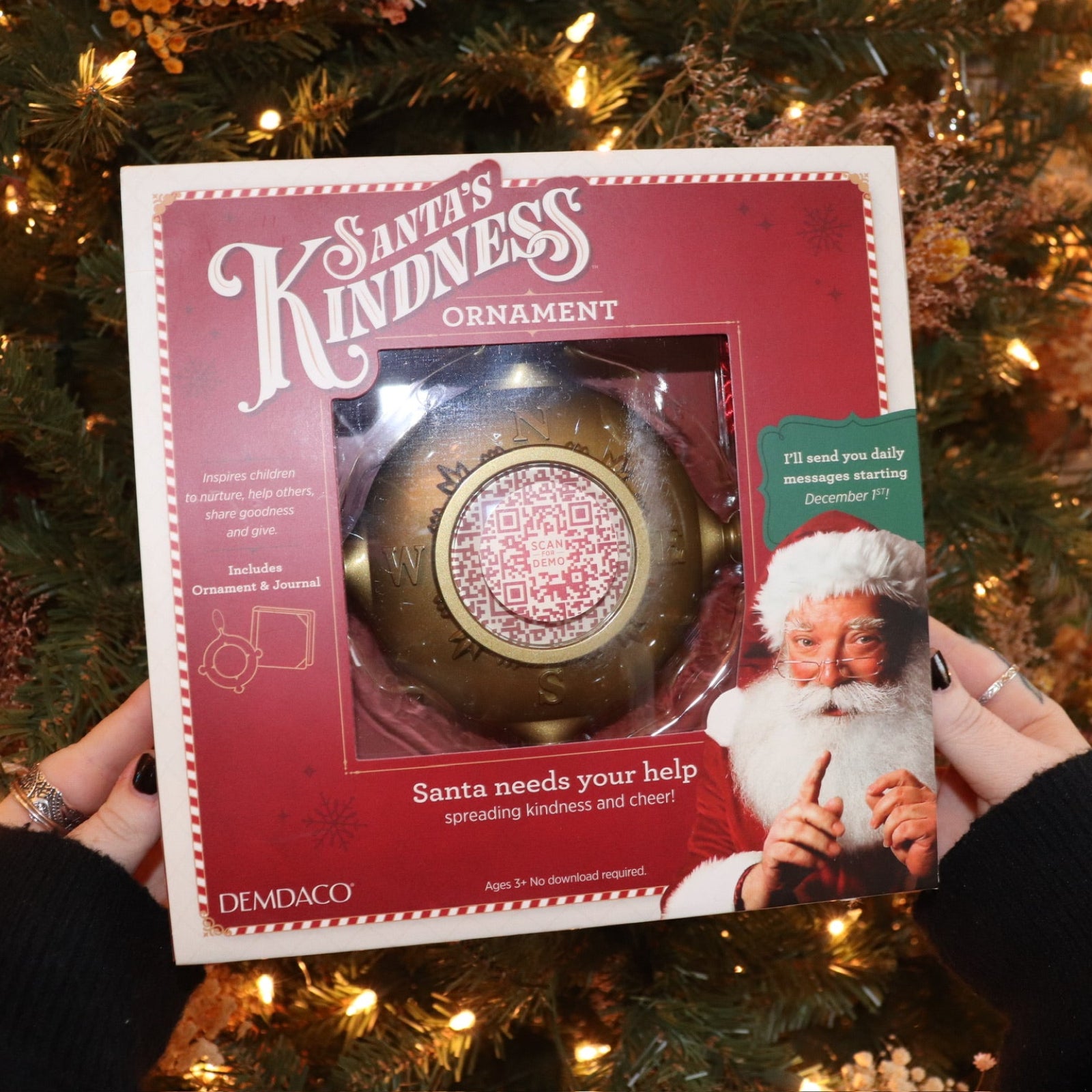 Someone holding the Santa's Kindness Ornament & Journal in front of a Christmas tree.