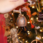 Someone holding the small Yuletide Protection Bell in front of a Christmas tree