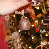 Someone holding the small Yuletide Protection Bell in front of a Christmas tree