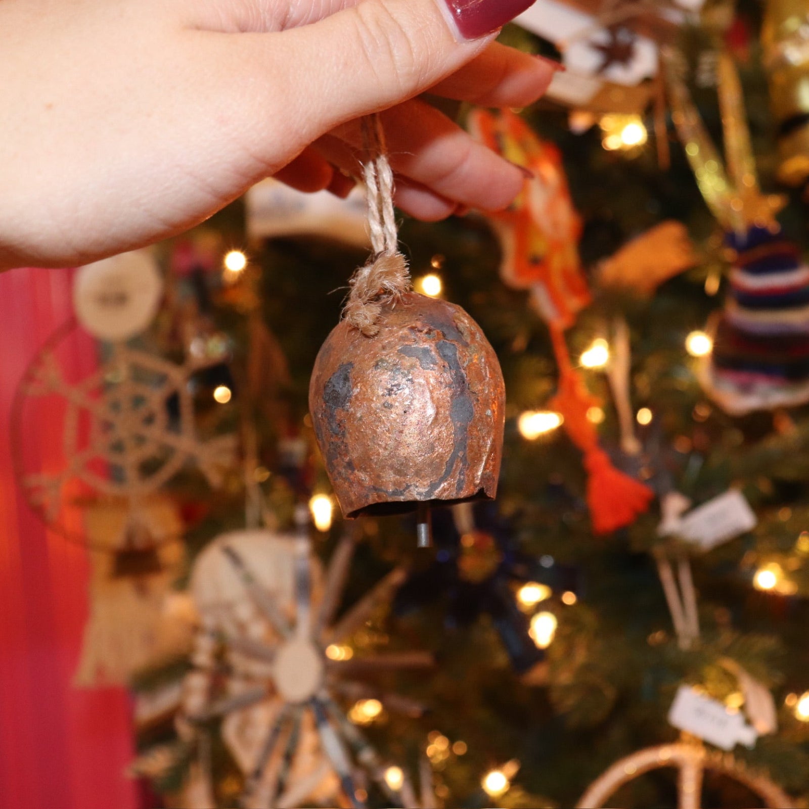 Someone holding the small Yuletide Protection Bell in front of a Christmas tree