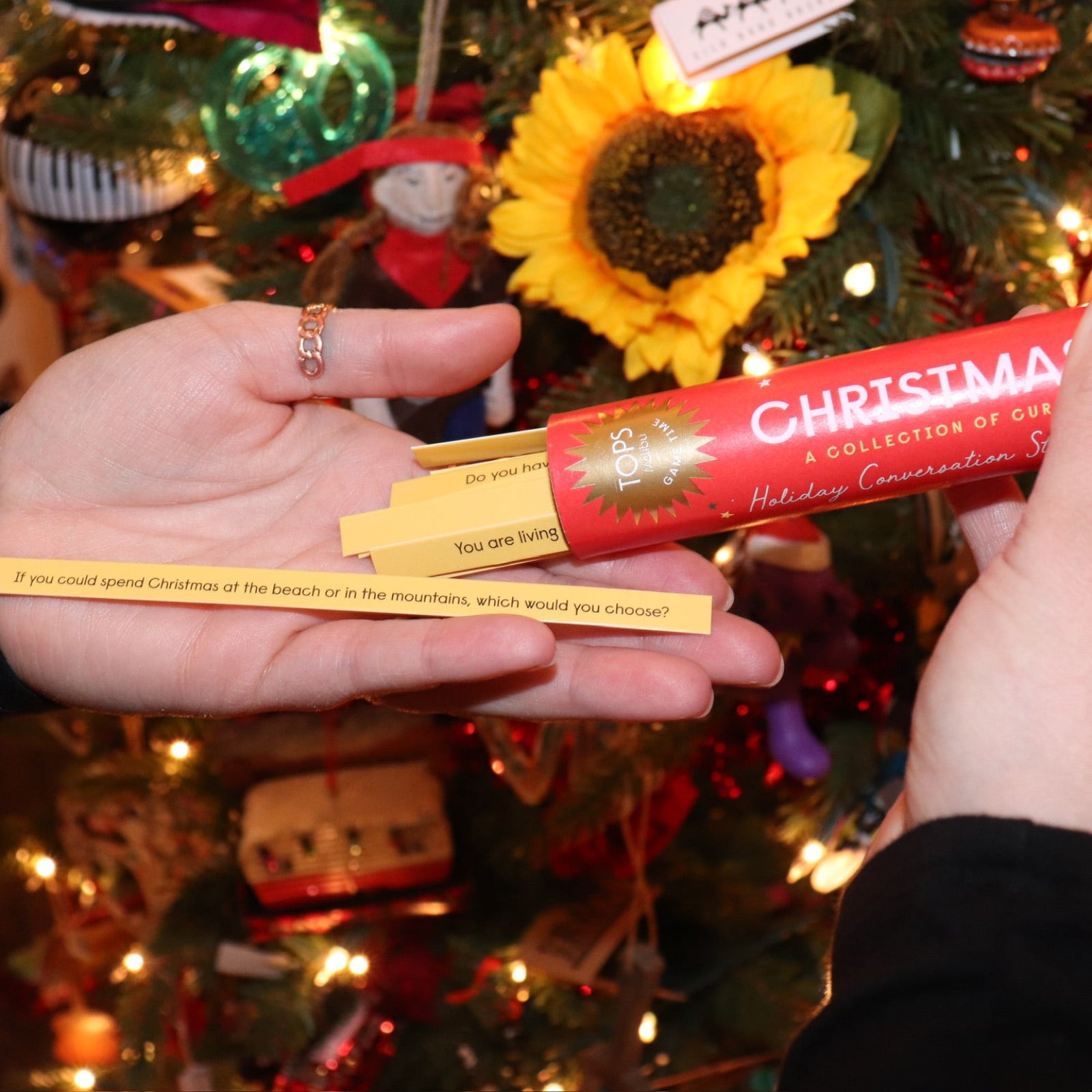 Someone holding the sticks from the Christmas Time Pick-up Sticks Conversation Game in front of a Christmas tree.