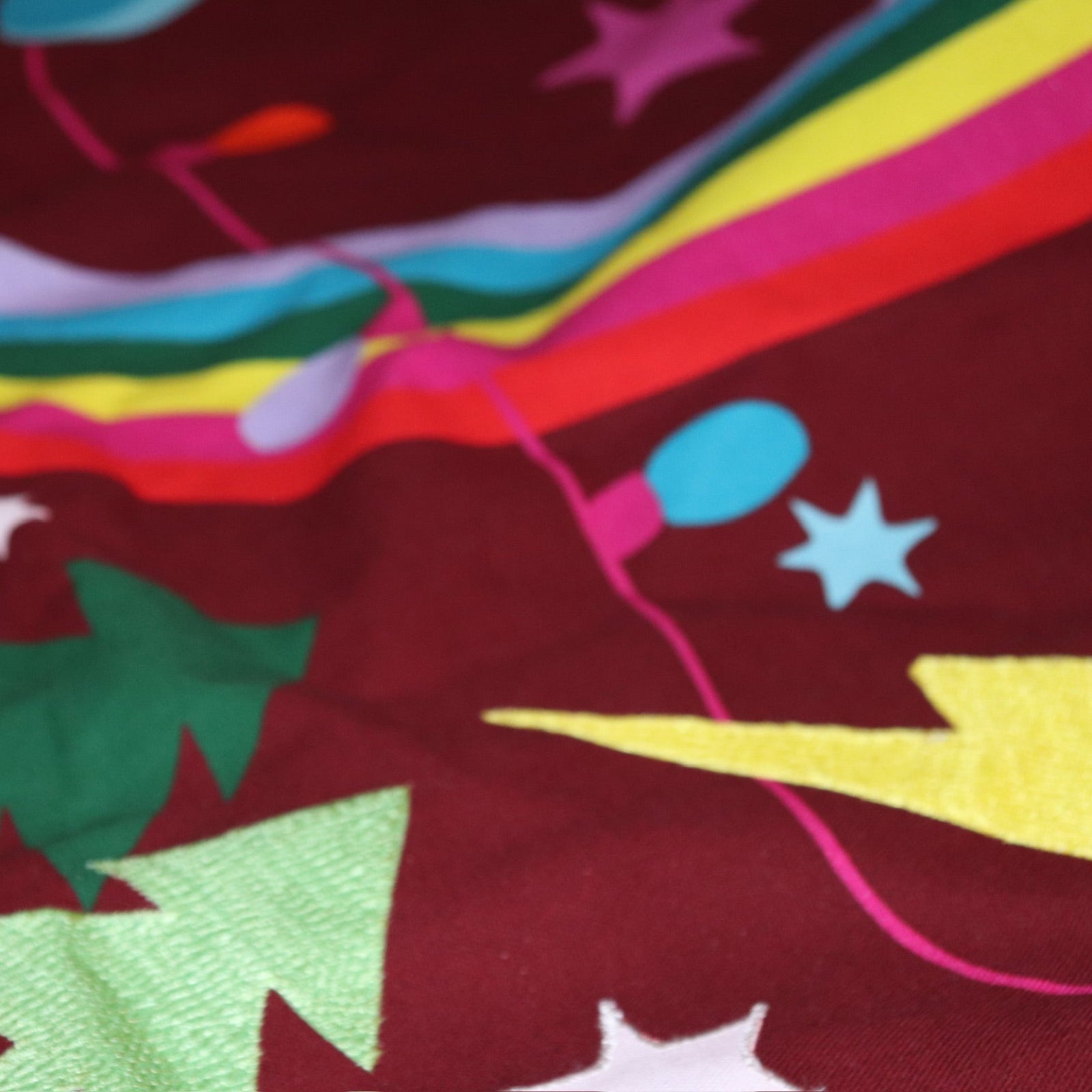 An up-close image of the All Is Bright Embroidered Tree Skirt around the bottom of a tree.