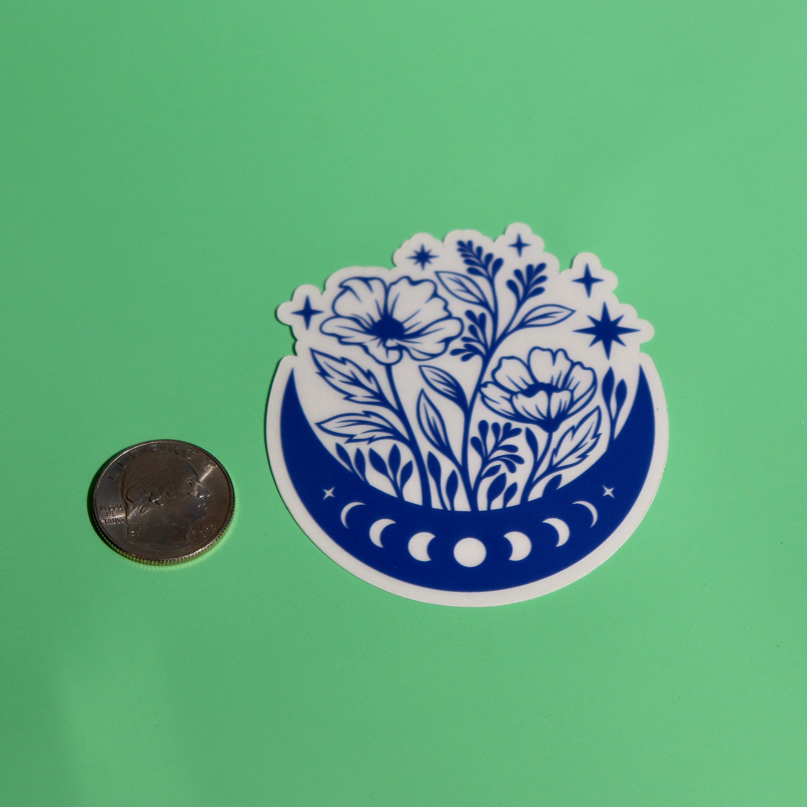 The Flower Moon Phase Sticker next to a quarter on a green background.
