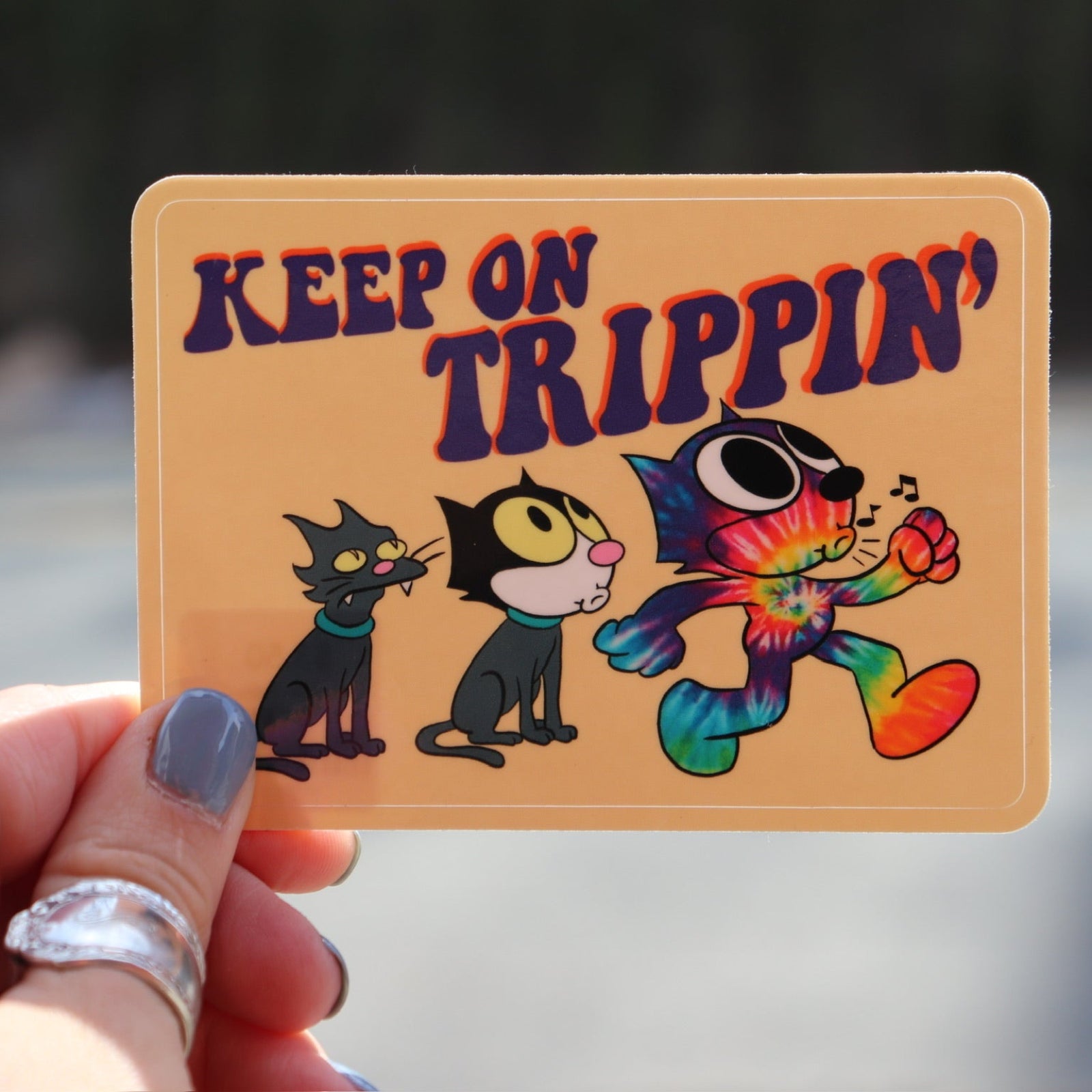 Someone holding the Keep On Trippin 4 Inch Sticker in front of a road.