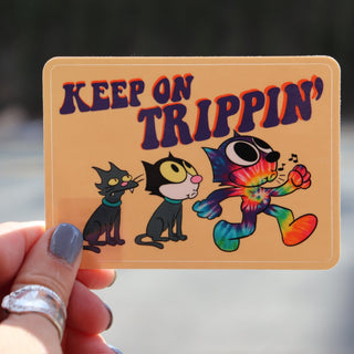 Someone holding the Keep On Trippin 4 Inch Sticker in front of a road.