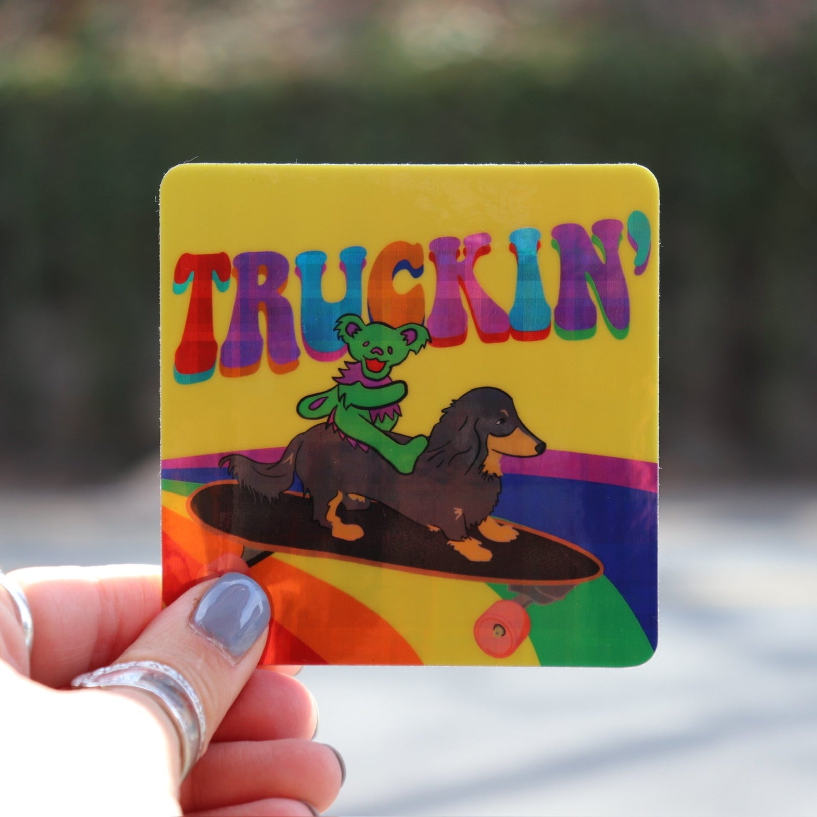 Someone holding the Truckin Grateful Dead Sparkle 3 Inch Sticker in front of a blurred road.