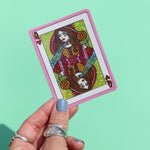 Someone holding the Queen of Hearts Glitter 3 Inch Sticker on a green background.