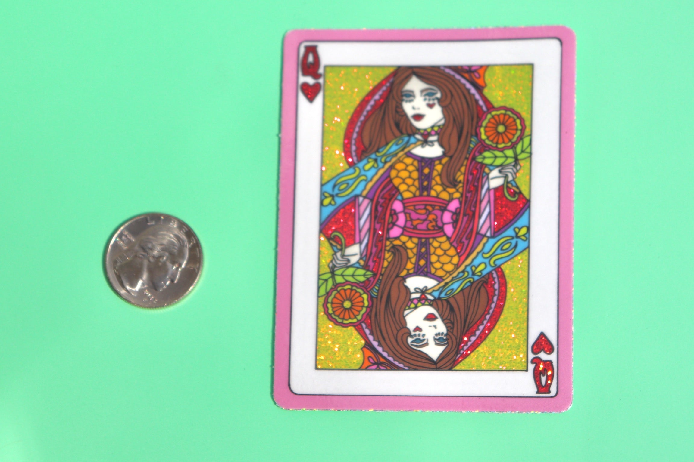 The Queen of Hearts Glitter 3 Inch Sticker next to a quarter on a green background.