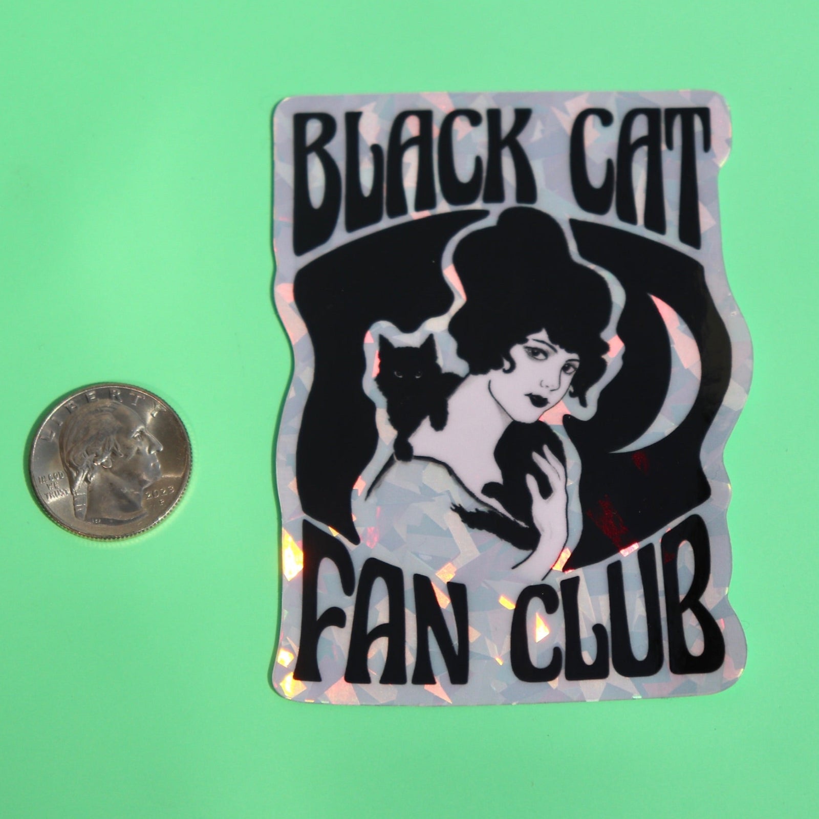 The Black Cat Fan Club 3 Inch Holographic Sticker next to a quarter on a green background.