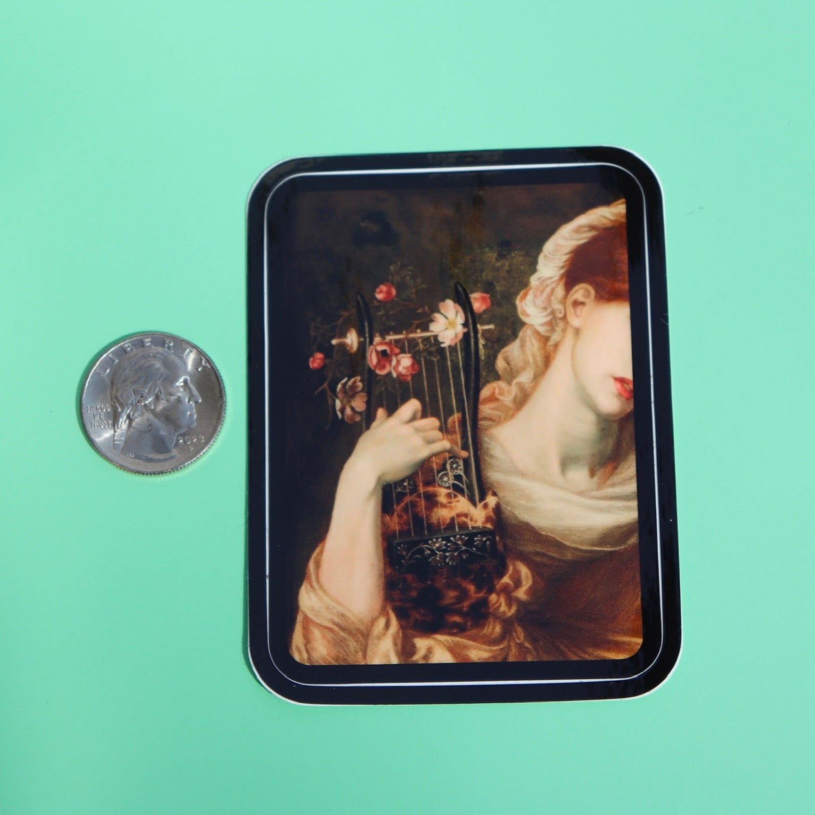 The Lyre Player Pre-Raphaelite 3 Inch Vinyl Sticker next to a quarter on a green background.