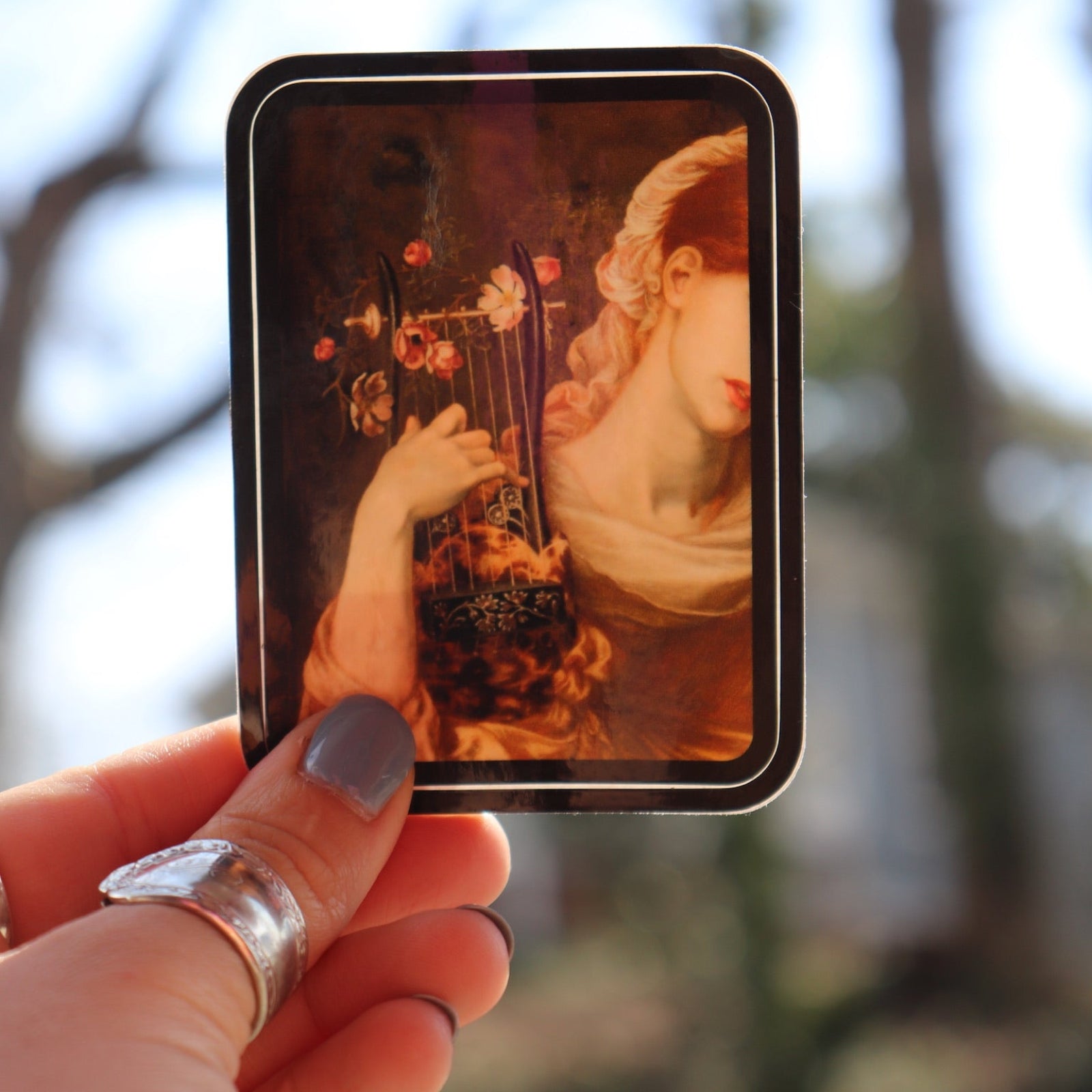 Someone holding the Lyre Player Pre-Raphaelite 3 Inch Vinyl Sticker.