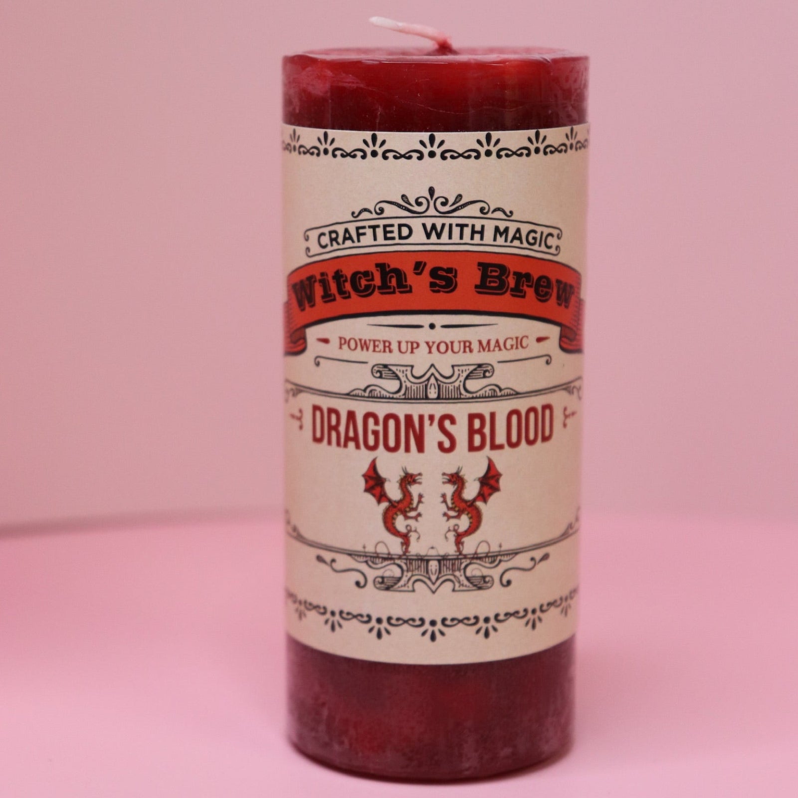 The Witch's Brew Dragon's Blood - Scented Pillar Candle on a pink background.