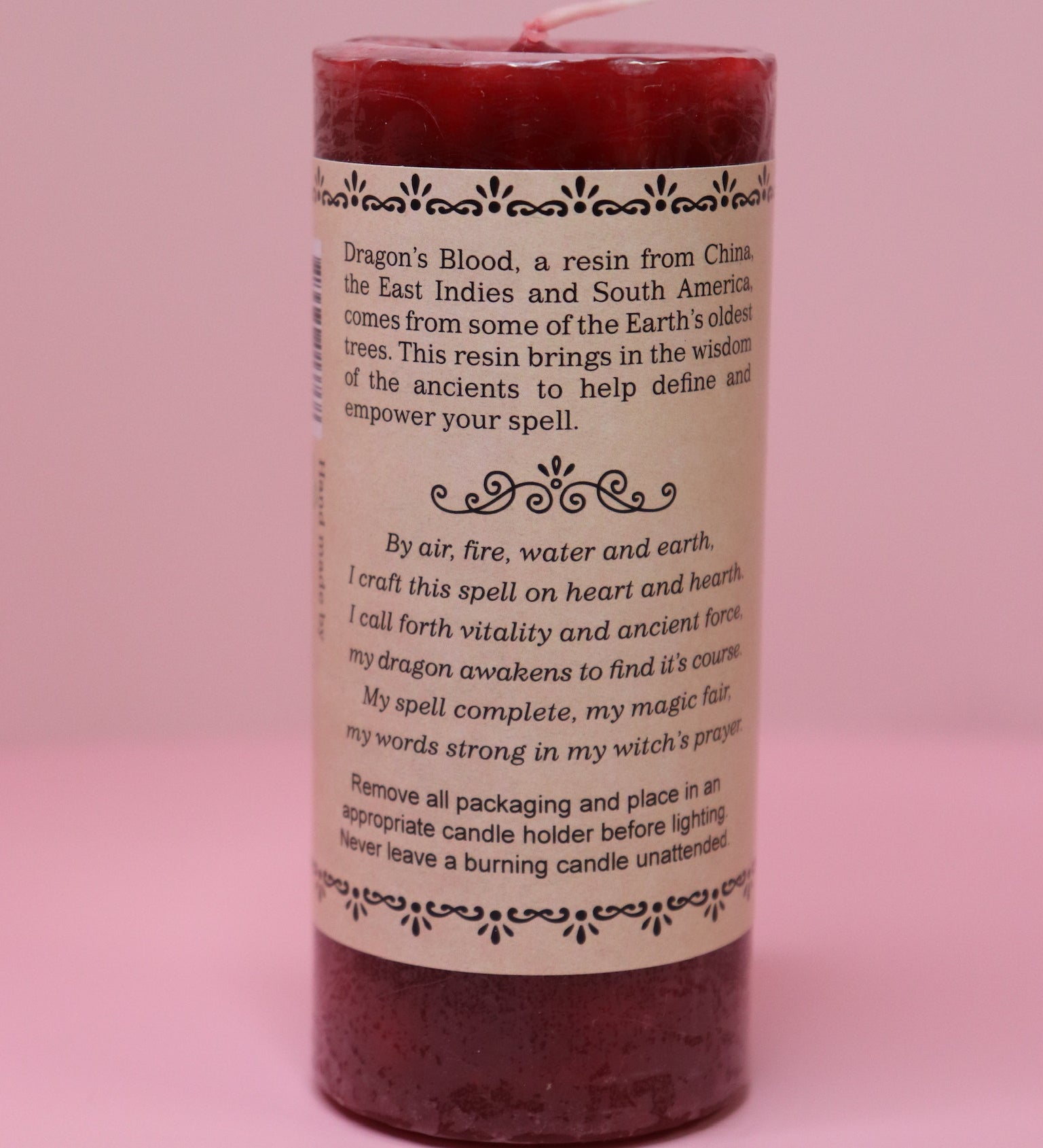 The back of the Witch's Brew Dragon's Blood - Scented Pillar Candle on a pink backgorund.