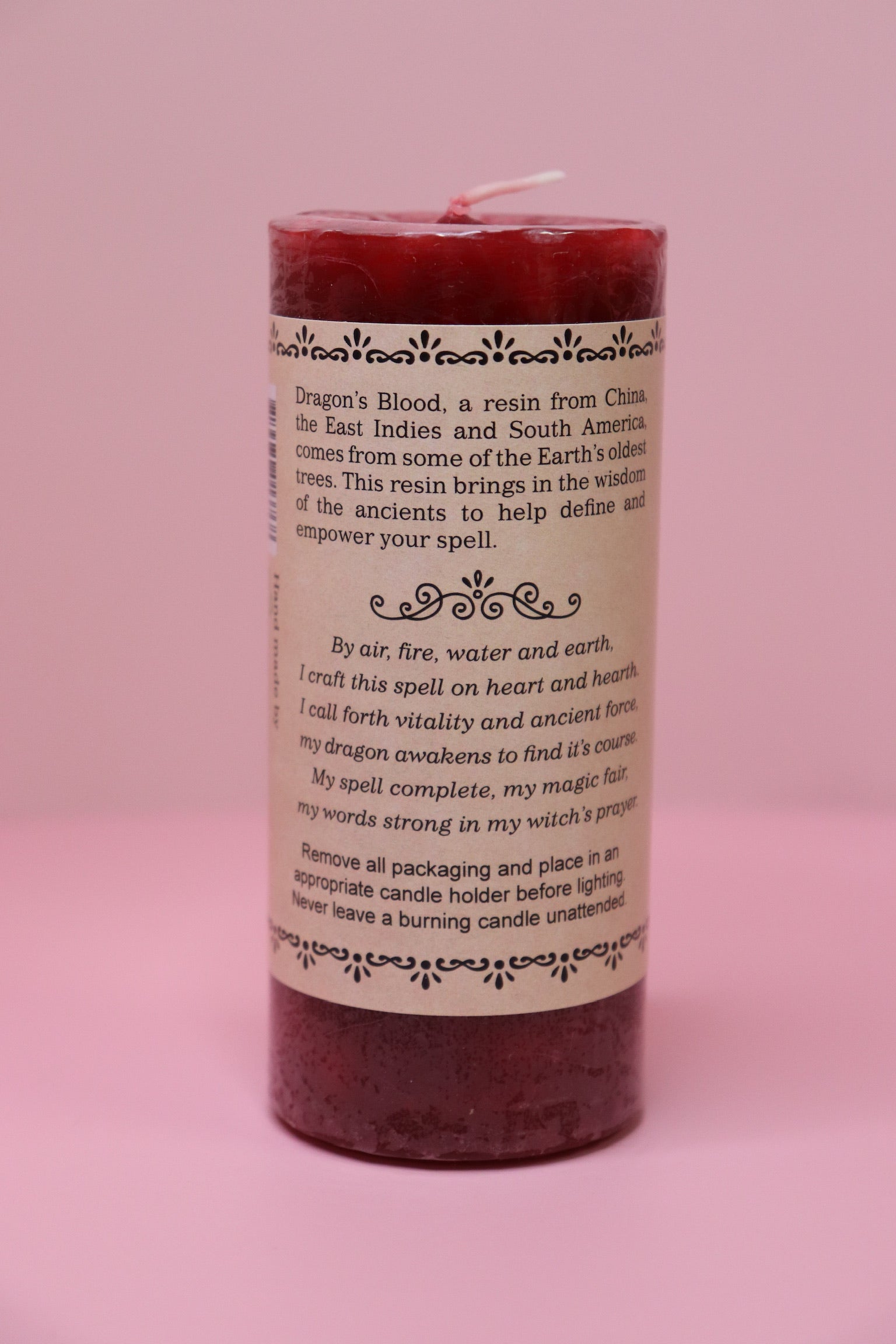 The back of the Witch's Brew Dragon's Blood - Scented Pillar Candle on a pink backgorund.